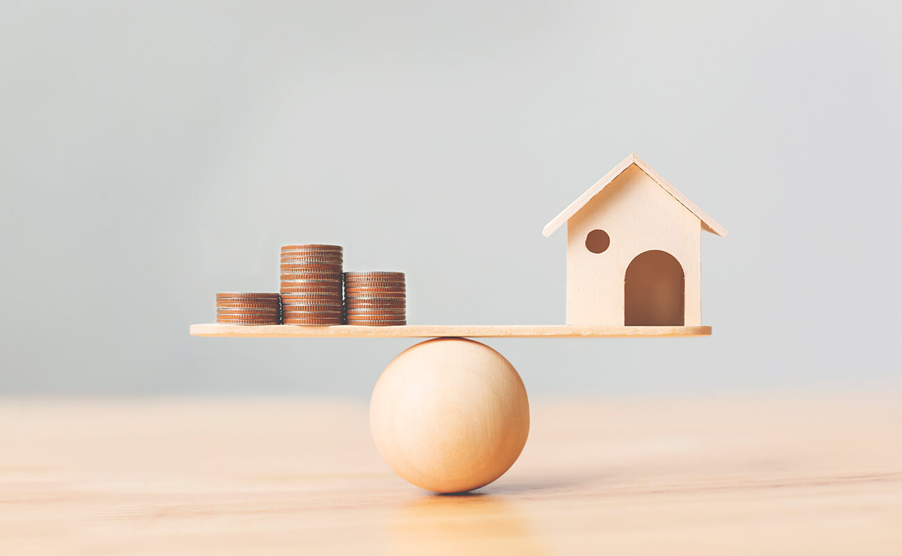 Petita casa de fusta i monedes equilibrades sobre una balança que simbolitzen la valoració immobiliària amb StyleHouse.